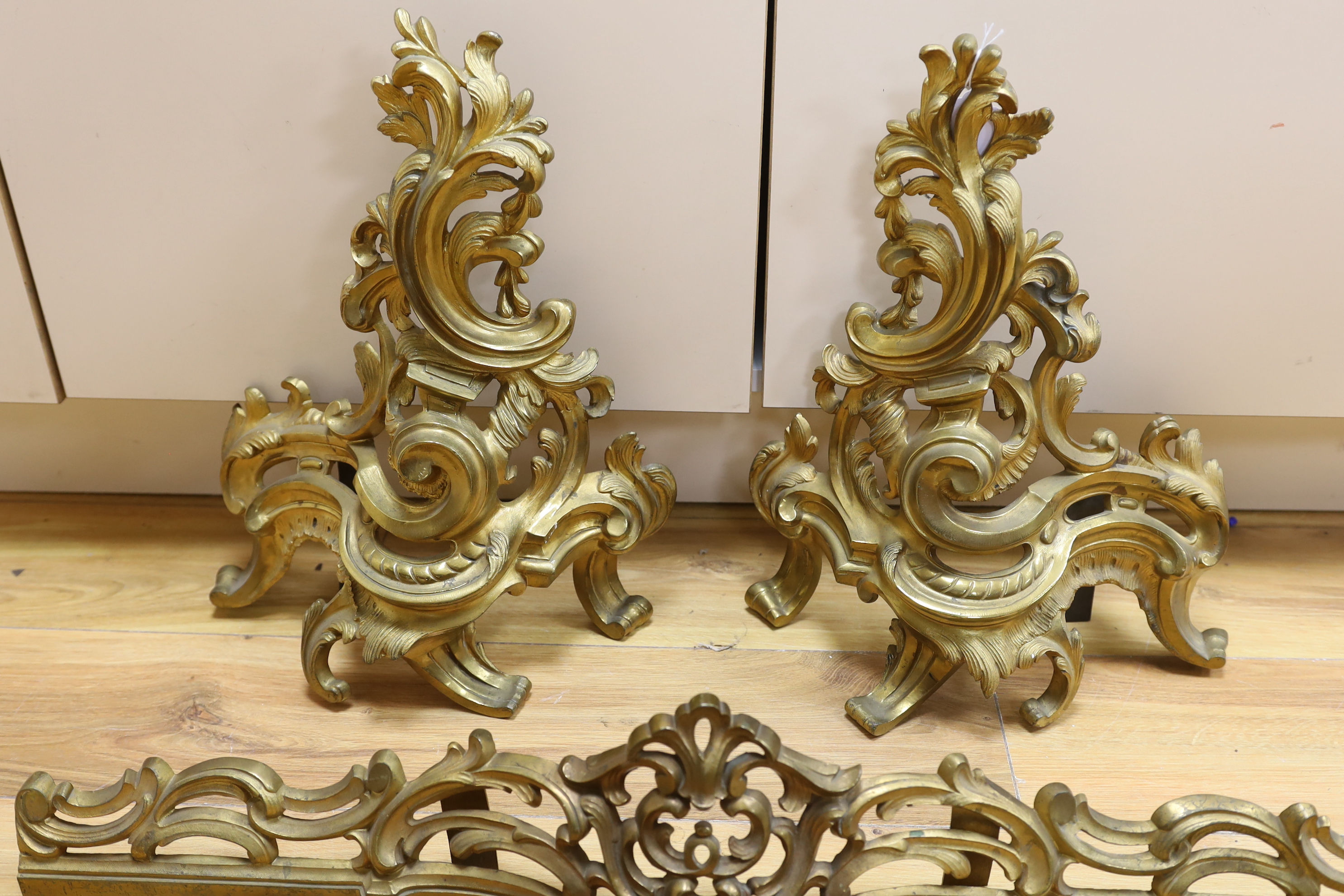 A French rococo revival gilt bronze fender with scroll work and bar, largest 44cm high